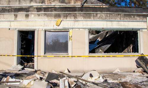A building storefront damaged by fire, and with a tape barrier stretched actoss the front.