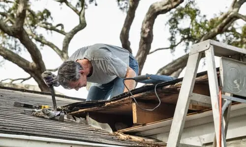 A man repairing the damage to his roof after a hurricane hit.