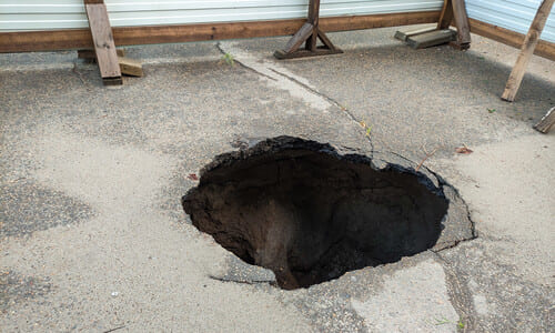 A sinkhole on a driveway blocked off with makeshift metal fences.
