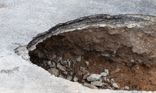 An angled shot of a wide sinkhole in the middle of a driveway 