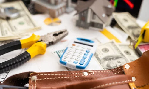 A model house, bank notes, and repair tools on a table next to a calculator.