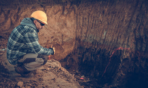 A geologist in a hardhat inspecting a very large sinkhole in the ground.